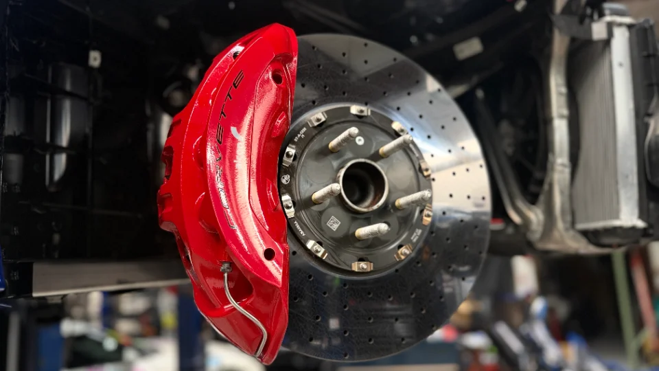 Close-up of a red Corvette brake caliper and drilled rotor, likely in a shop environment.