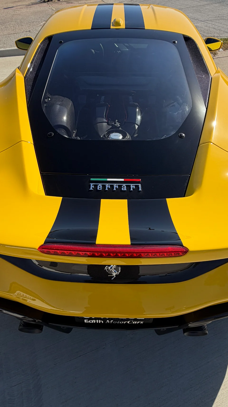 Rear view of a yellow Ferrari supercar with black racing stripes, showcasing its engine bay and carbon fiber details.