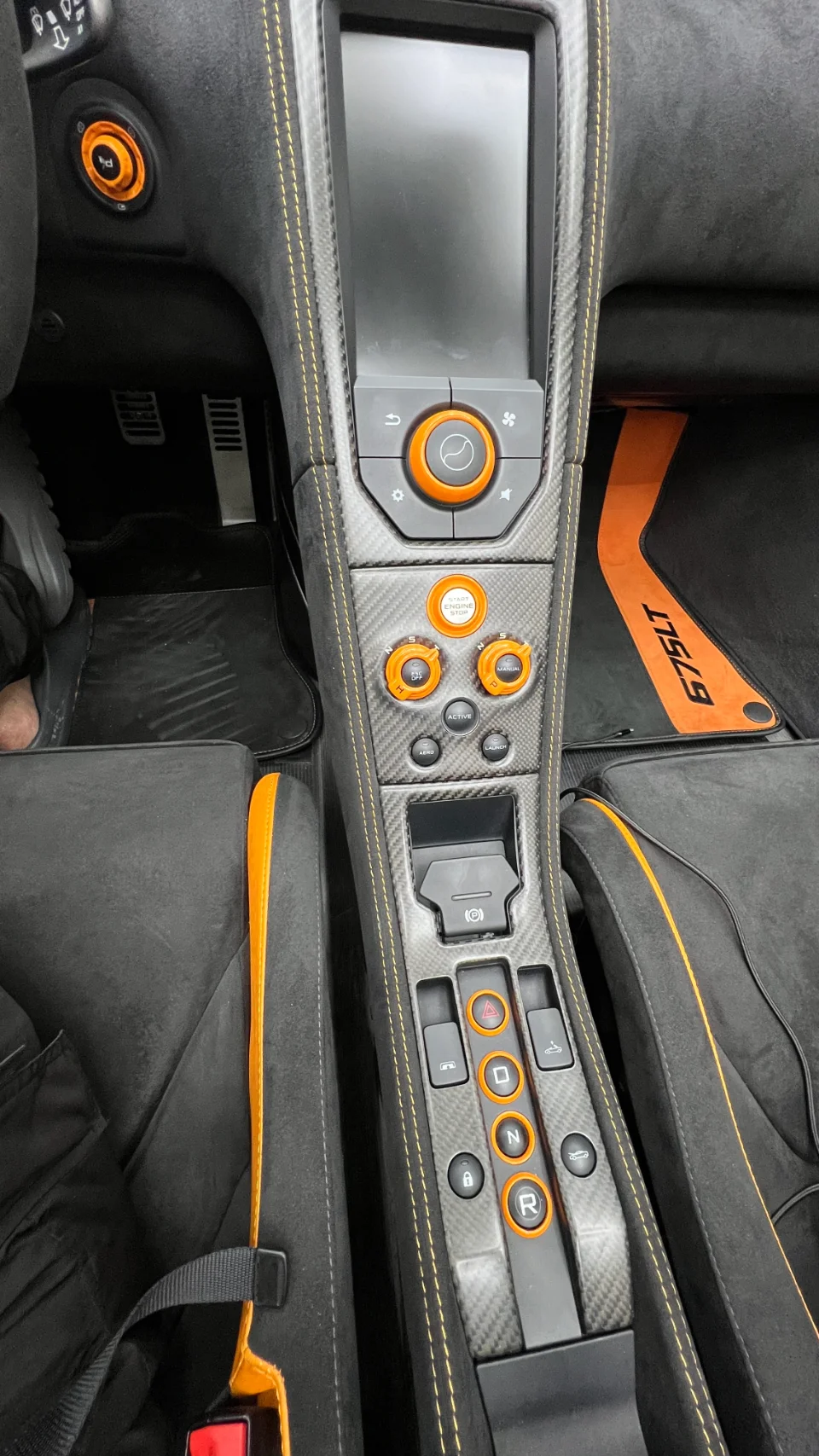 A detailed view of a McLaren 675LT interior, showcasing the carbon fiber center console, orange accents, and Alcantara trim.