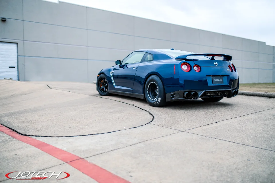A blue Nissan GT-R R35 with drag tires and an aftermarket exhaust system parked in front of a building.