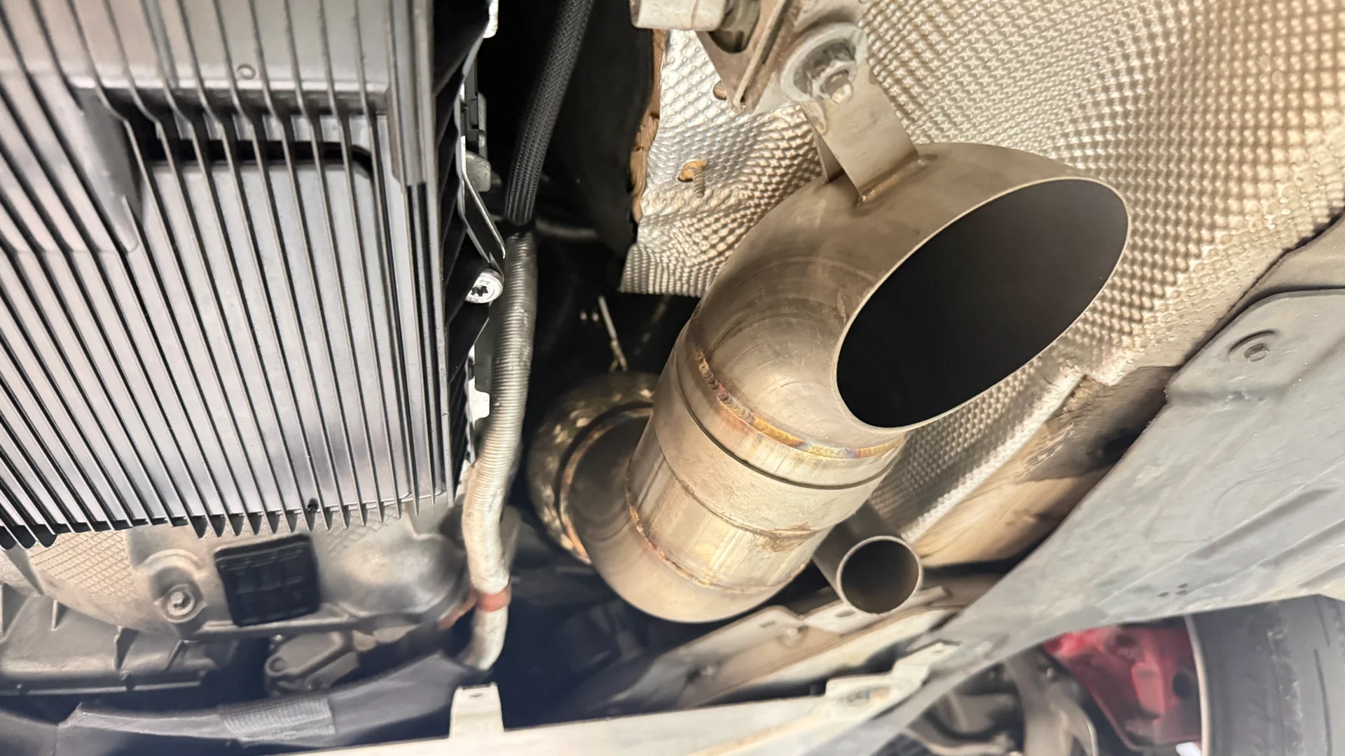 Close-up view of a custom stainless steel exhaust system and downpipe installed on the underside of a performance car.