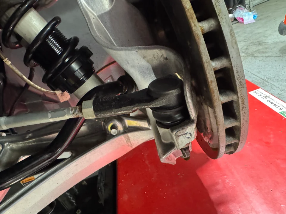Close-up view of a car's suspension, brake rotor, and steering components being worked on in a shop.