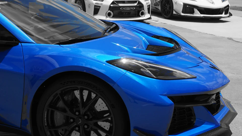 A vibrant blue Chevrolet Corvette Z06 with black wheels parked, with a white Nissan GT-R visible in the background.