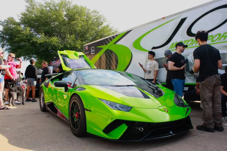 A bright green Lamborghini Huracan with its engine bay open, parked at an outdoor car event with people and a Jotech Motorsports trailer.