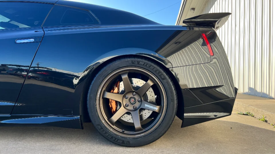 A black Nissan GT-R R35 with bronze Volk TE37 wheels and Brembo brakes parked outdoors, showcasing its rear quarter.