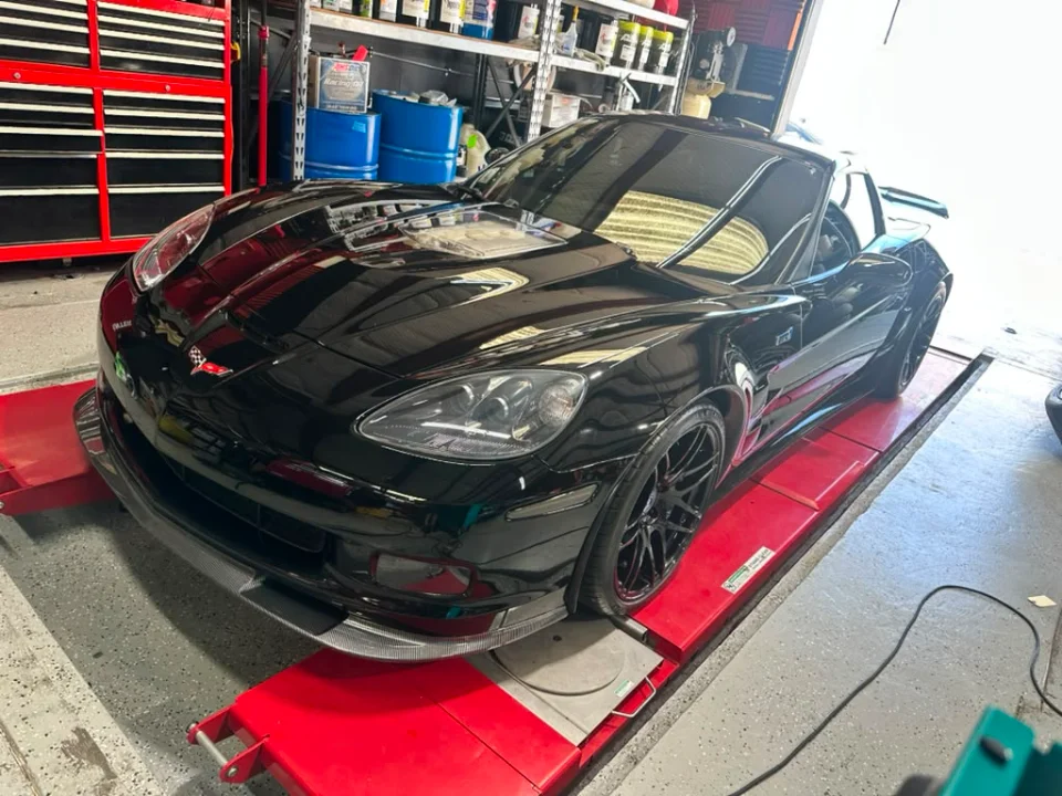Black C6 Corvette Z06 on a red dyno in a performance tuning shop, ready for power testing.