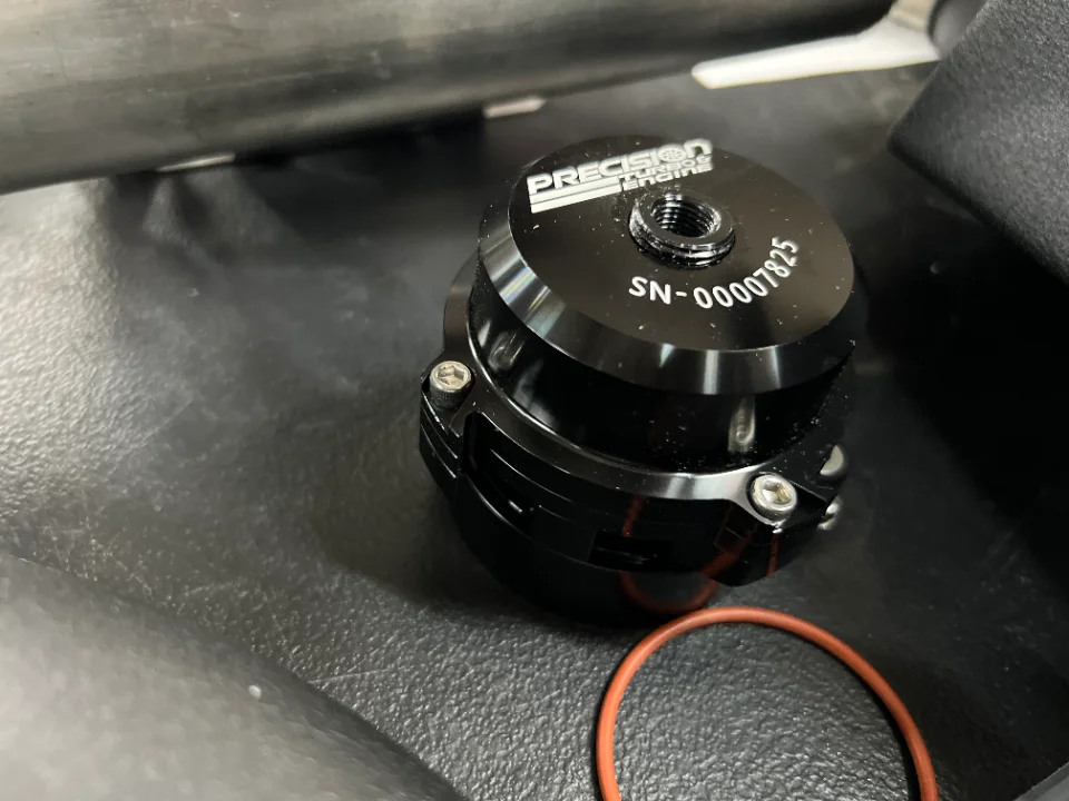 Close-up of a black Precision Turbo & Engine blow-off valve with a serial number and an orange O-ring.
