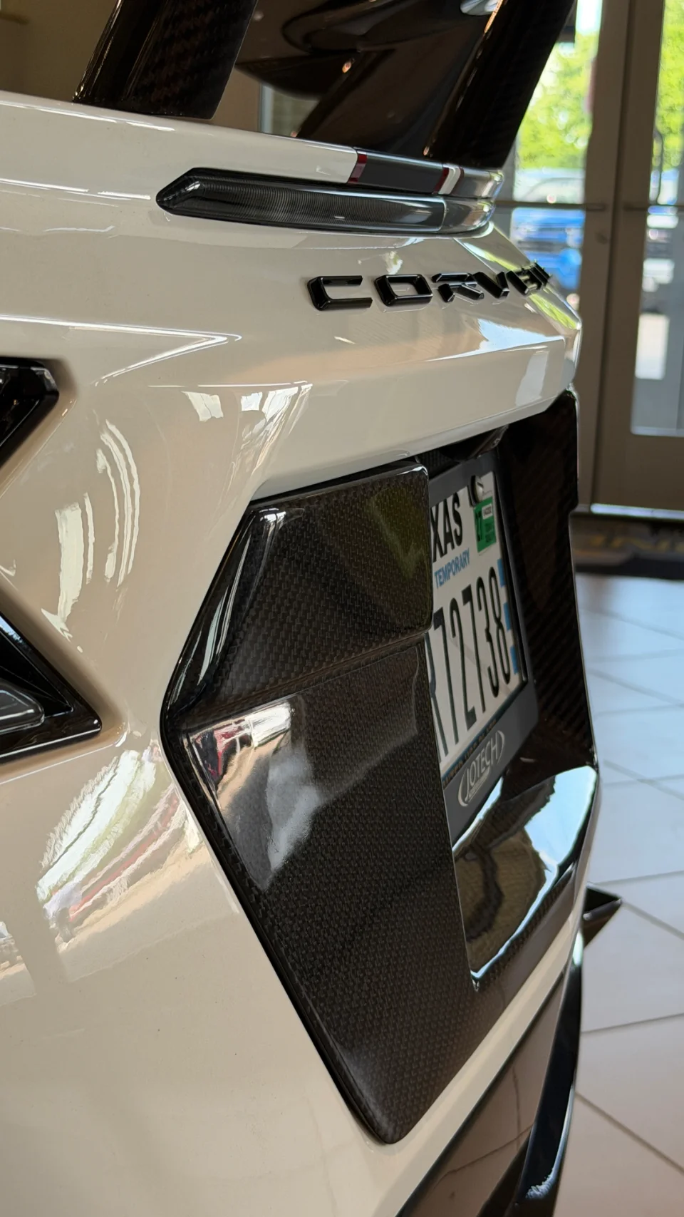 Close-up of the rear of a white Corvette, showcasing its carbon fiber rear wing, diffuser, and Texas temporary license plate.