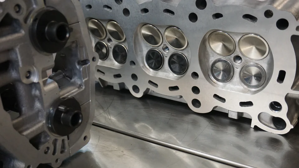 Close-up of a disassembled engine cylinder head with visible valves on a metallic workbench, ready for assembly or service.