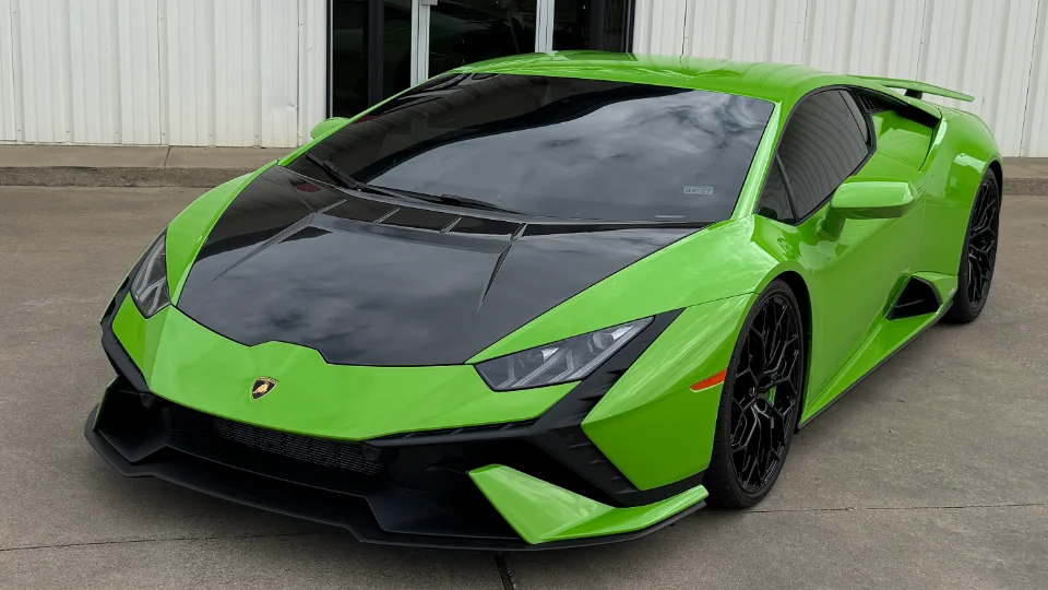 A vibrant green Lamborghini Huracan with a black carbon fiber hood and black wheels parked outside a building.