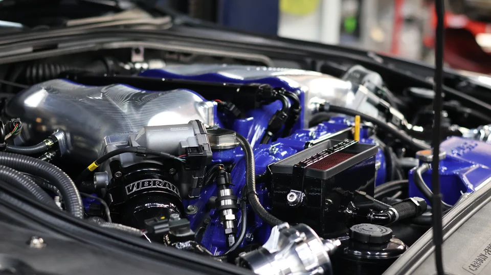 Close-up of a high-performance engine bay featuring a blue intake manifold, polished components, and custom fuel lines.