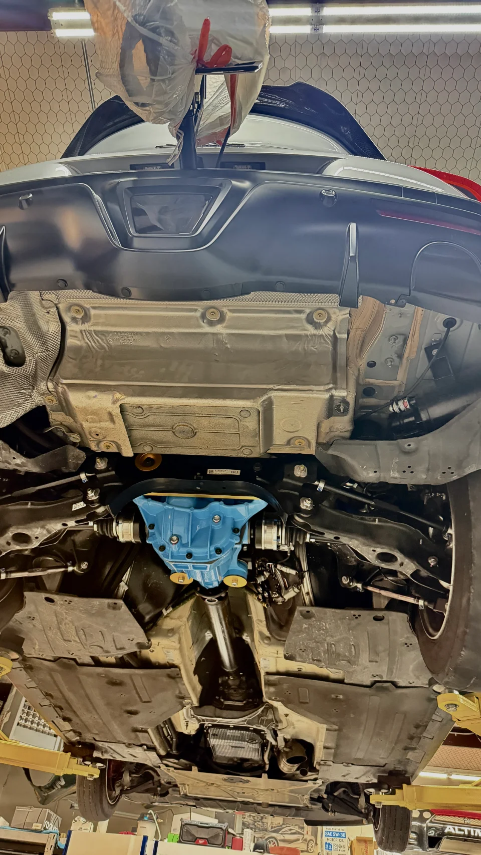 Underside view of a car on a lift in a shop, showcasing a blue aftermarket differential and drivetrain components.