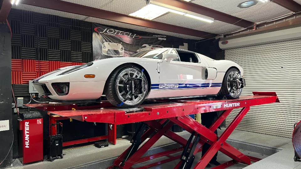 A white Ford GT with blue racing stripes on a red Hunter alignment rack inside the Jotech Motorsports shop.