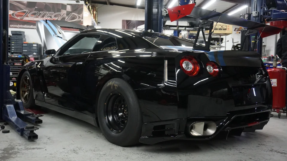 Black Nissan GT-R with a large aftermarket wing and drag tires in the Jotech Motorsports shop.