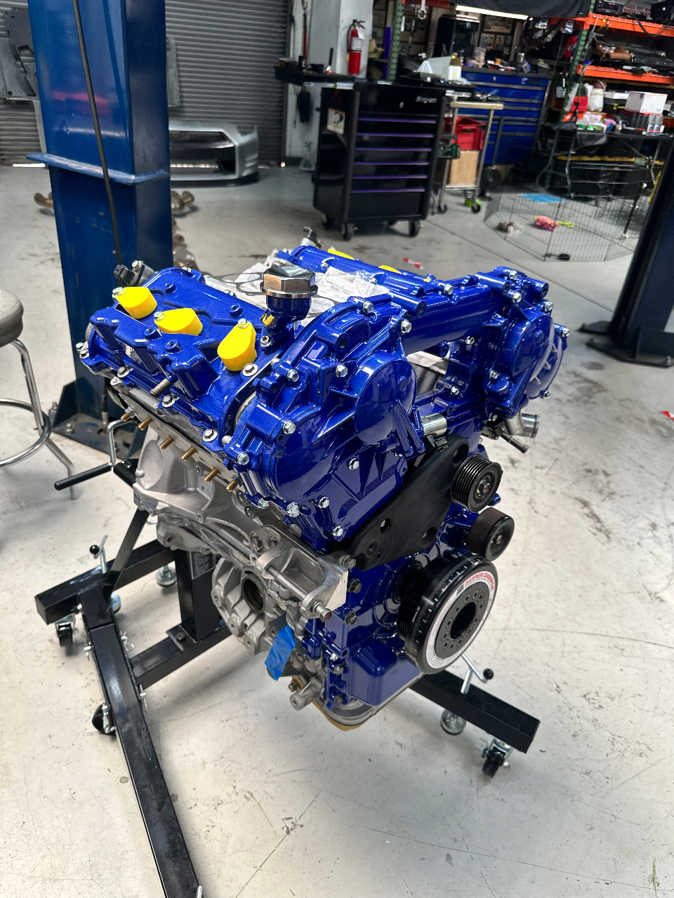 A freshly built engine with bright blue valve covers and components, mounted on an engine stand in a professional automotive shop.