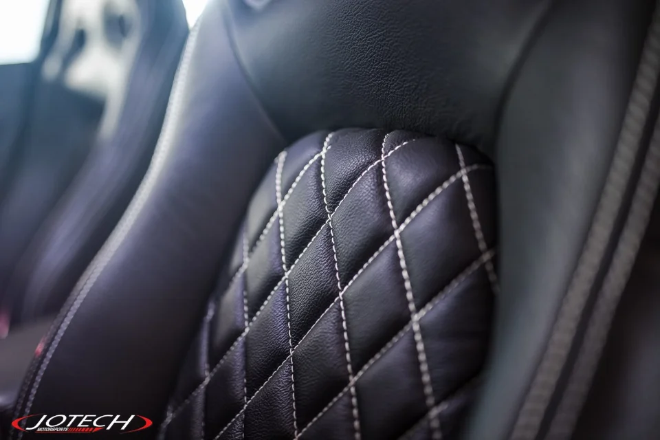 Close-up of a black leather car seat with white diamond stitching, showcasing interior detail.