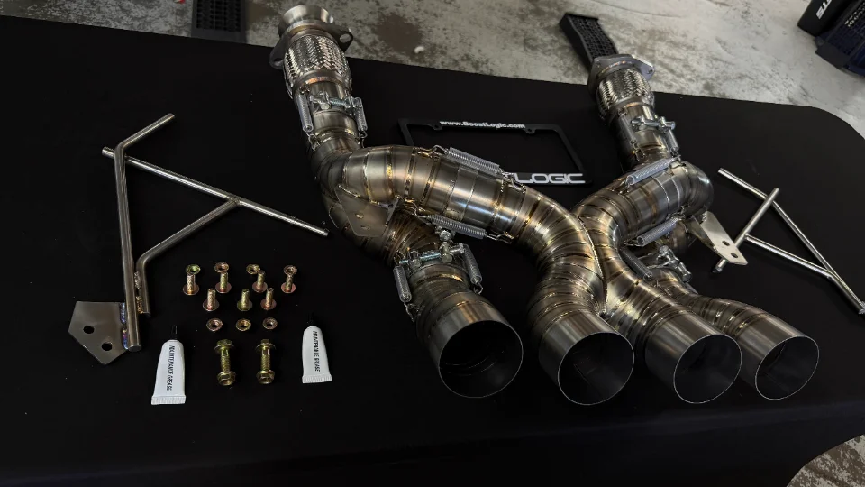Boost Logic titanium exhaust system with hardware and mounting accessories on a black surface.