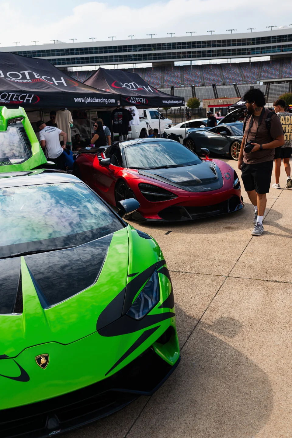 A vibrant green Lamborghini and a red McLaren supercar parked at a Jotech Motorsports event with people and tents.