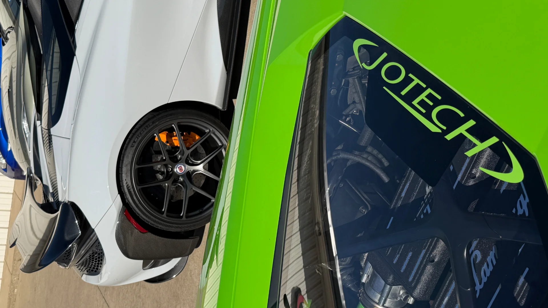 Close-up of a green Lamborghini with Jotech branding next to a white McLaren with custom wheels and orange brake calipers.