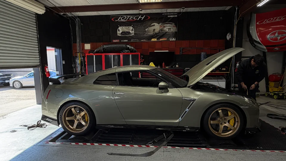 A Nissan GT-R on a dyno at Jotech Motorsports with its hood open, being worked on by a technician.