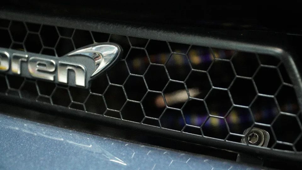 Close-up detail of a McLaren car's front grille featuring the iconic McLaren logo and honeycomb mesh.