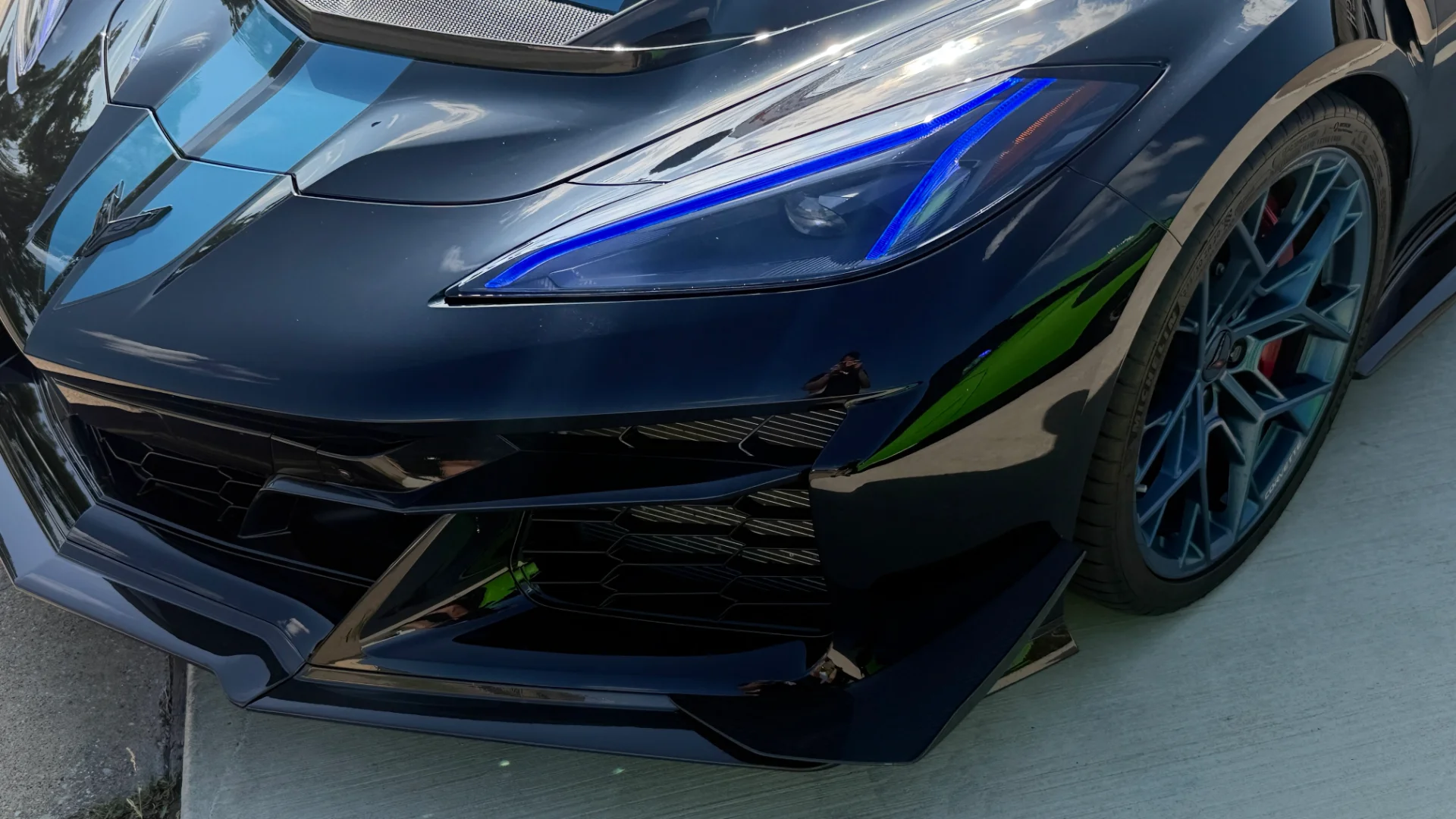 Close-up of a black Corvette C8 front end with blue racing stripes, custom blue wheels, and illuminated blue headlights.