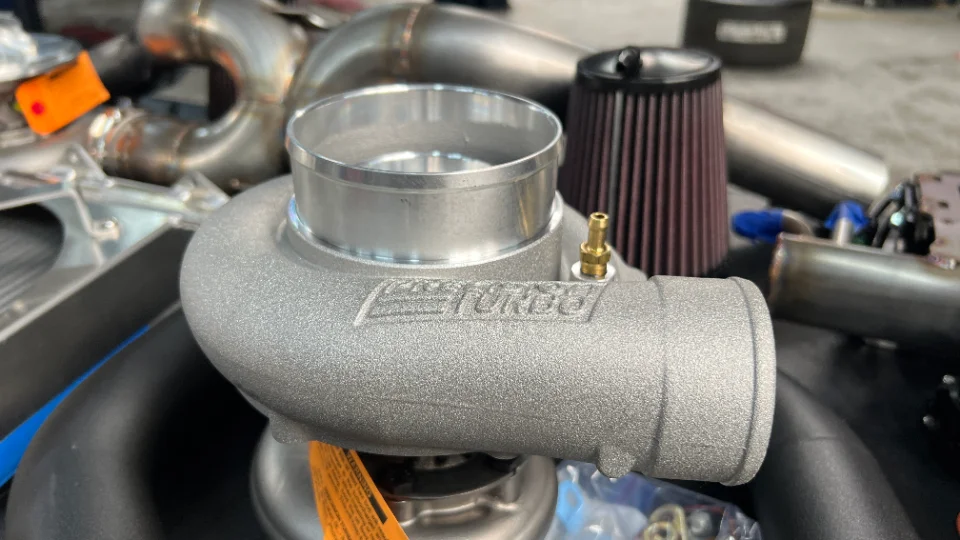 A close-up of a new turbocharger with an air filter and exhaust piping in the background, ready for installation.