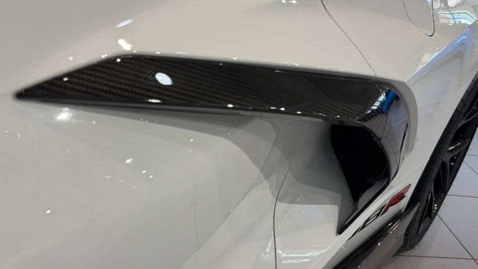 A close-up of a white C8 Corvette Z06's rear quarter panel, highlighting the carbon fiber side vent.