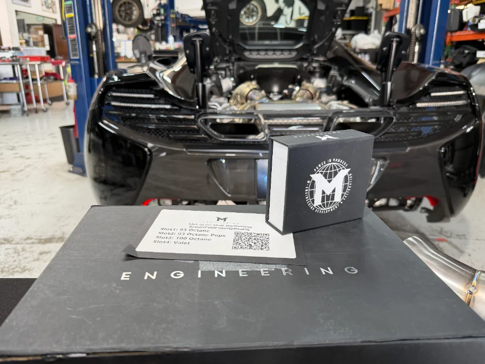 M-Engineering ECU tuning products and packaging displayed in a performance shop with a McLaren sports car.
