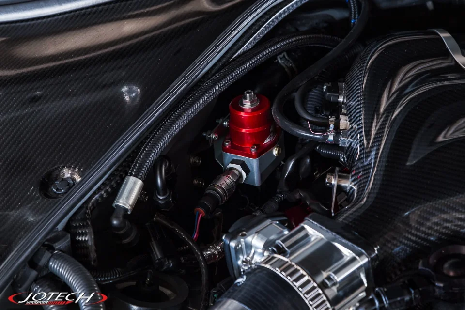 Close-up of a red aftermarket fuel pressure regulator and carbon fiber components in a high-performance engine bay.