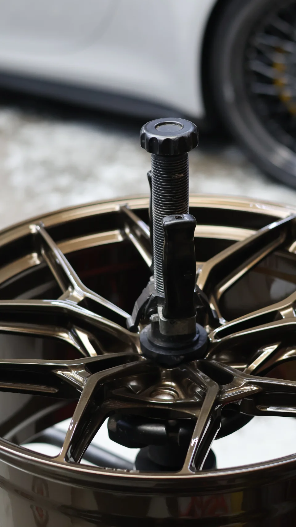 Close-up of a bronze multi-spoke wheel mounted on a tire machine in a shop setting.