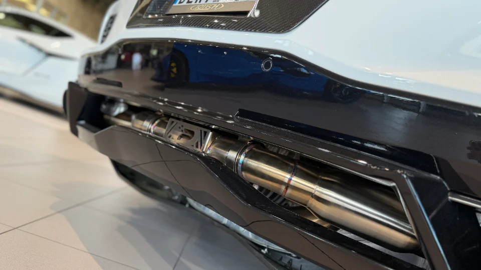 Close-up of a Jotech Motorsports aftermarket titanium exhaust system visible through the rear bumper of a white Corvette C8.