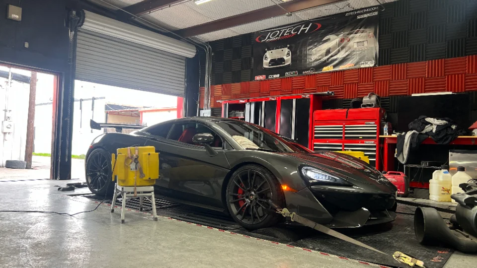 Grey McLaren supercar strapped to a dynamometer in a performance tuning shop with Jotech branding visible.
