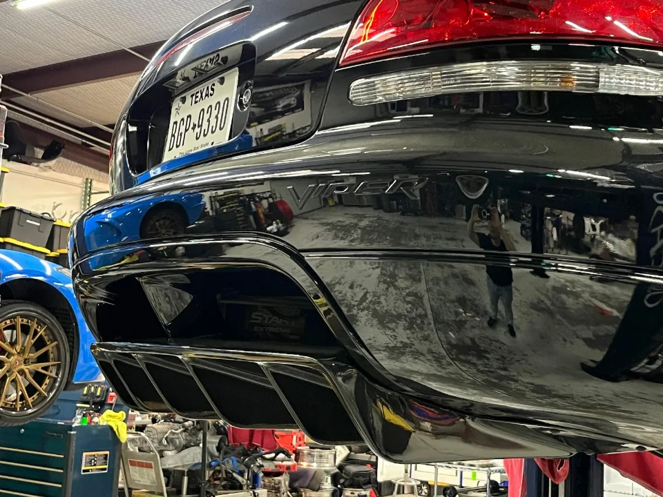 A black Dodge Viper on a lift, showcasing its rear diffuser and exhaust tips in a shop environment.