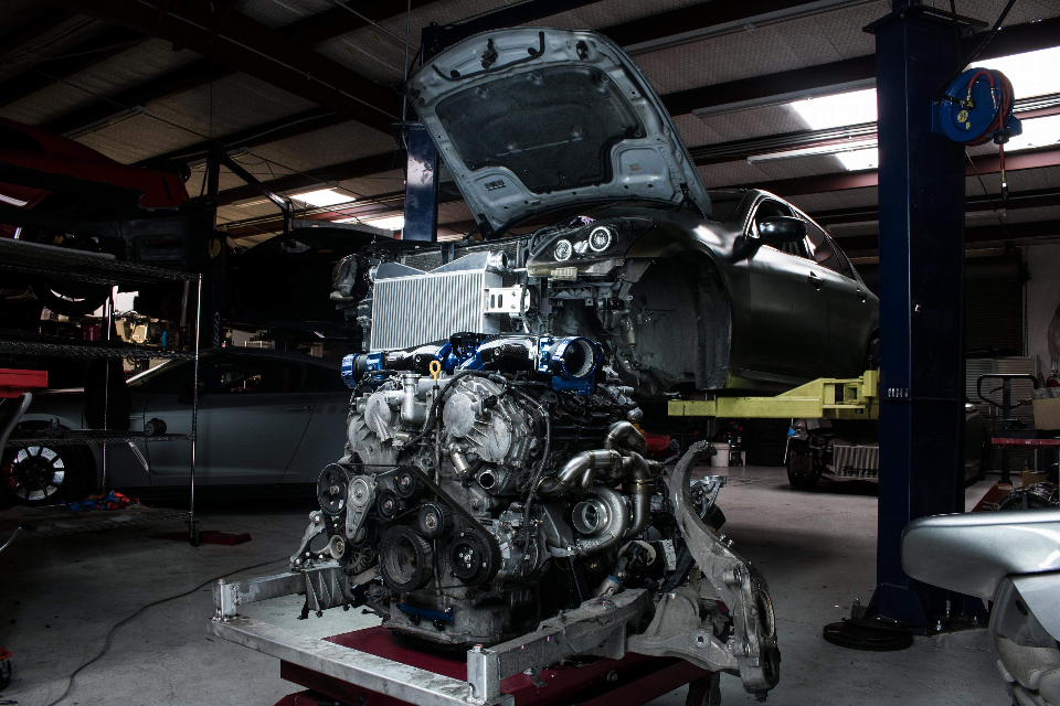 A detailed view of a car engine with twin turbos and an intercooler removed from a vehicle in a performance shop.