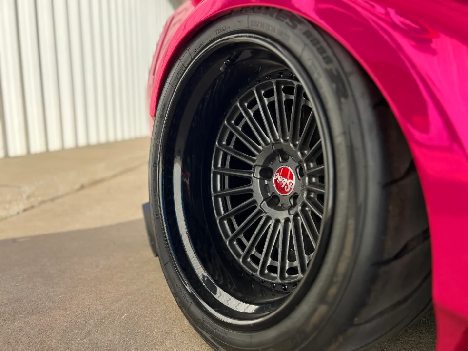 Close-up of a pink custom car's black multi-spoke wheel and tire, showcasing the fitment.