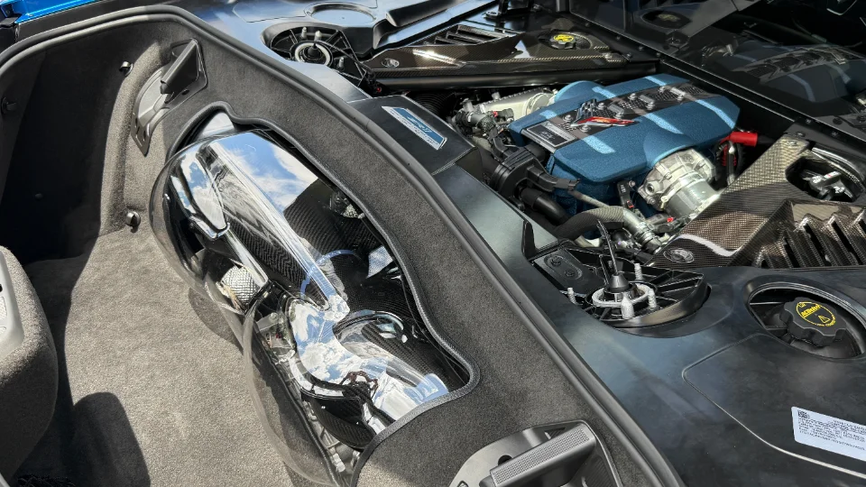 Close-up view of a Corvette C8 engine bay featuring the LT2 engine with a blue cover and carbon fiber intake components.