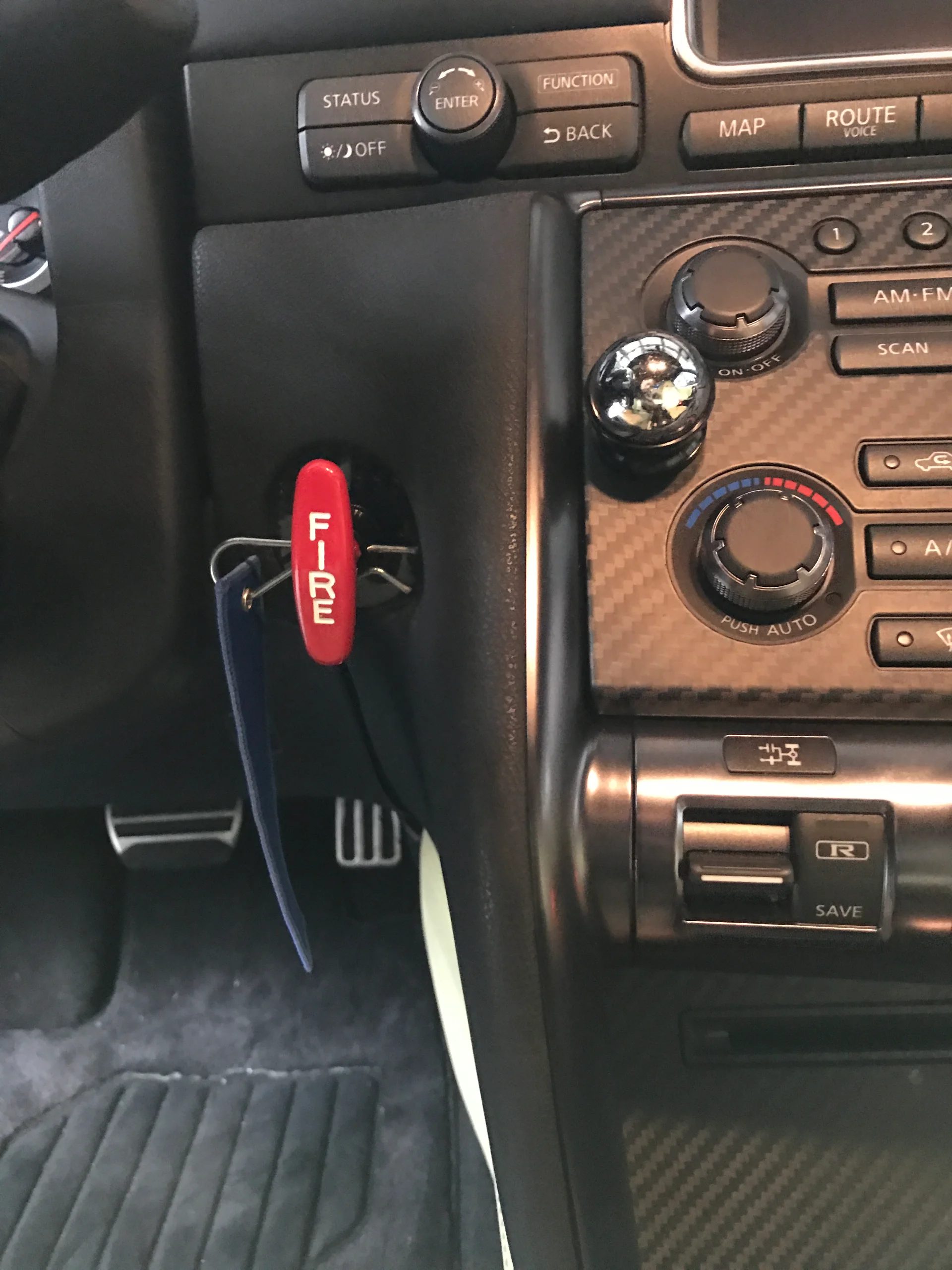 Close-up of a Nissan GT-R interior showing the center console, pedals, and a red 'FIRE' pull handle for a fire suppression system.