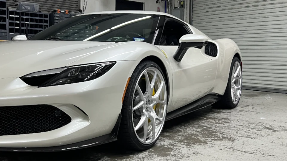 A white Ferrari supercar with custom silver HRE wheels and yellow brake calipers, parked inside a clean garage or shop.