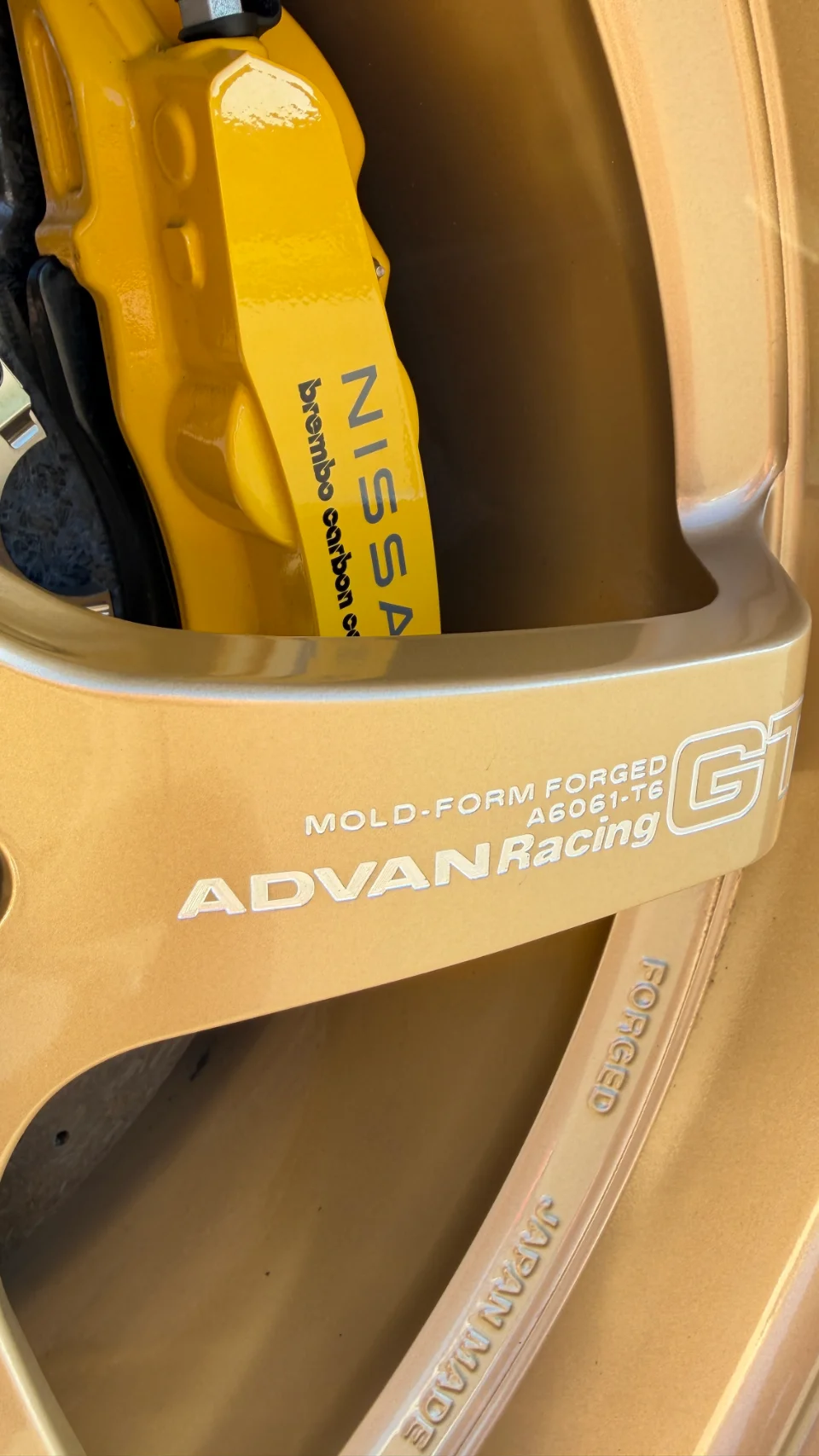 Close-up of a gold Advan Racing GT wheel with a yellow Nissan Brembo carbon ceramic brake caliper.
