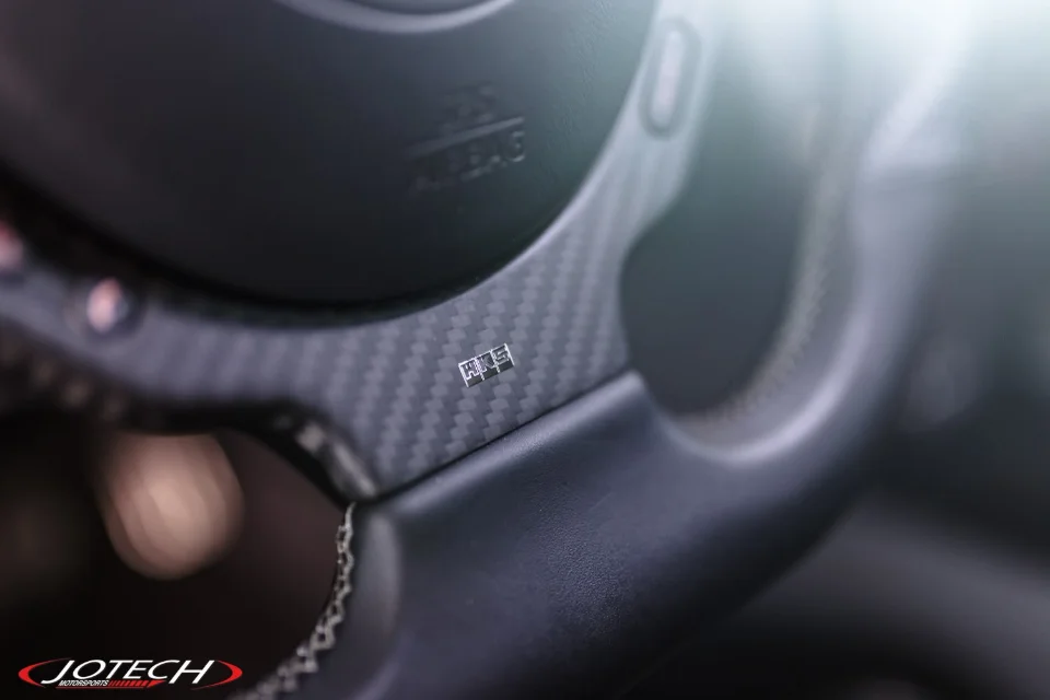 Close-up of a car's carbon fiber steering wheel with an HKS badge, showcasing interior detail.