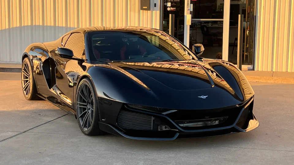 A sleek black custom supercar parked outside a building, showcasing its aggressive front design and glossy finish.
