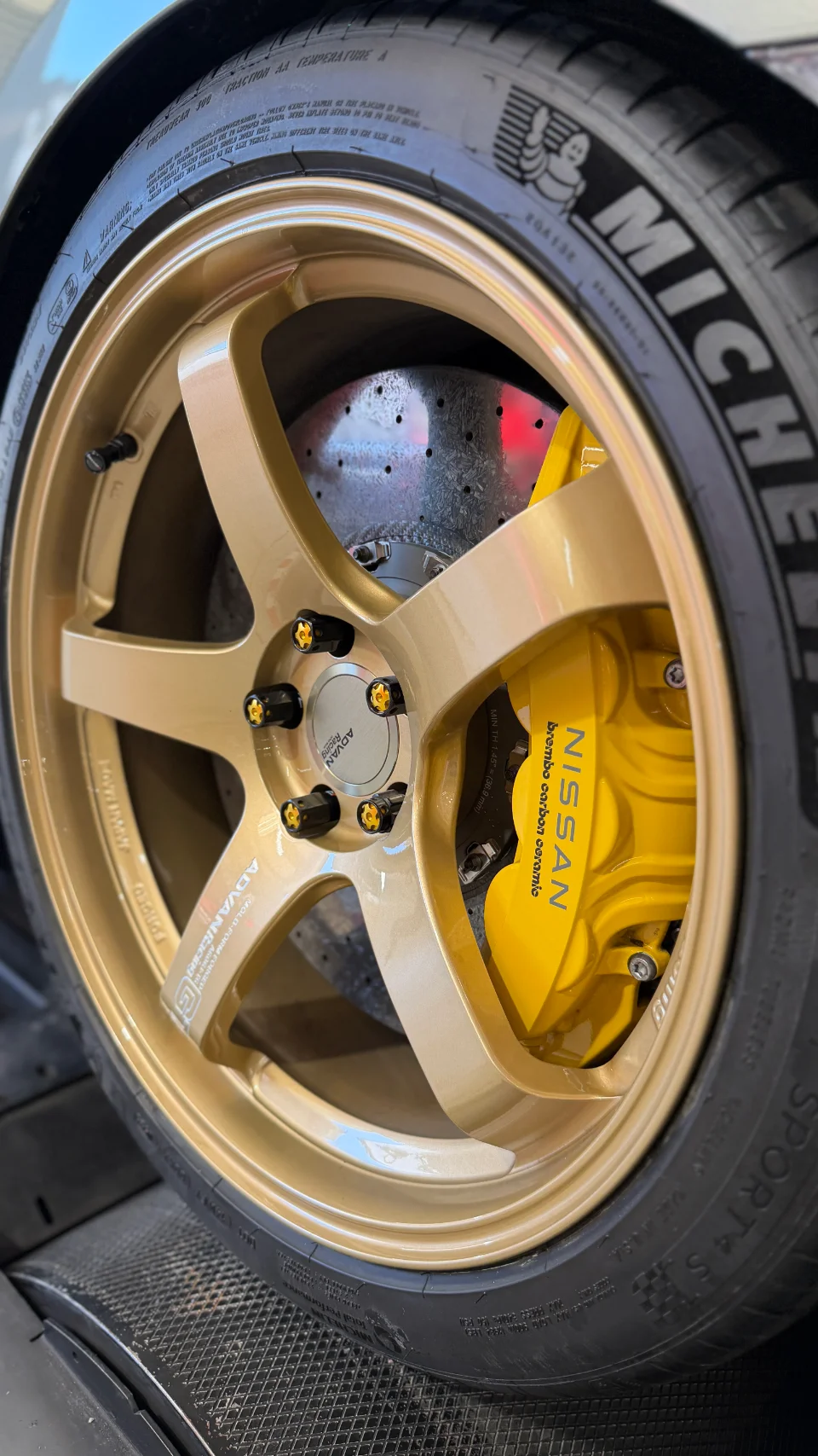 Close-up of a Nissan GT-R's gold Advan Racing wheels, Michelin tires, and yellow Brembo carbon ceramic brakes.