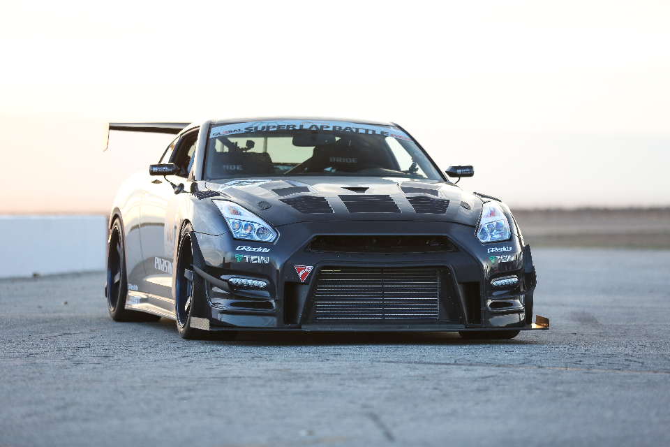 Highly modified Nissan GT-R track car with widebody kit, carbon fiber hood, and large front splitter on a track.