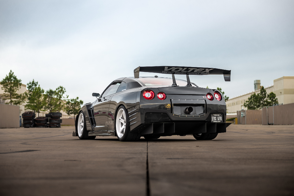 Rear view of a grey widebody Nissan GT-R with a large Voltex rear wing and custom diffuser parked on an asphalt lot.