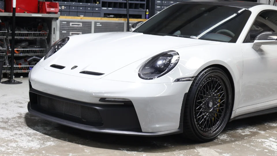 White Porsche 911 GT3 with aftermarket multi-spoke wheels showcased in a performance shop.