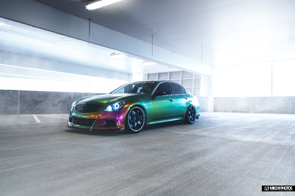 Infiniti G37 sedan with a vibrant chameleon wrap and aftermarket wheels parked in a concrete garage.