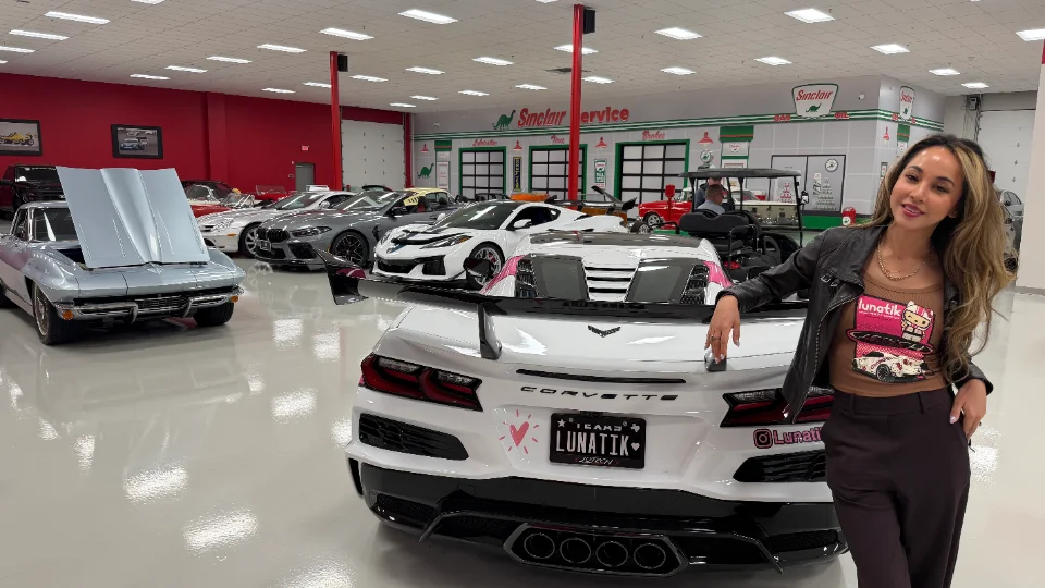 A woman poses in a car showroom with a white Corvette C8 Z06, a classic silver Corvette, and other performance cars.