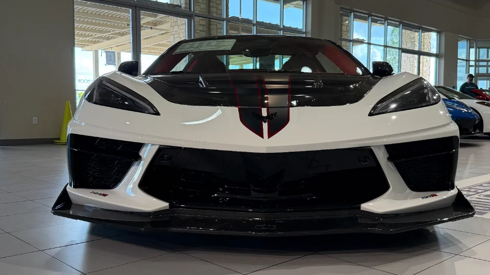 Front view of a white Corvette C8 with black and red racing stripes and carbon fiber aero in a showroom.