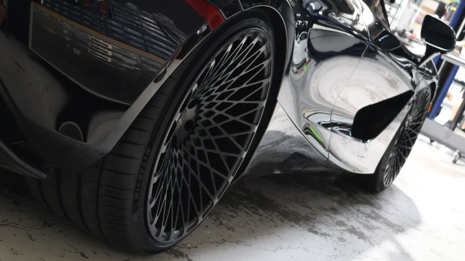 Close-up of a black McLaren's rear wheel with intricate custom spokes and performance tires in a clean shop environment.